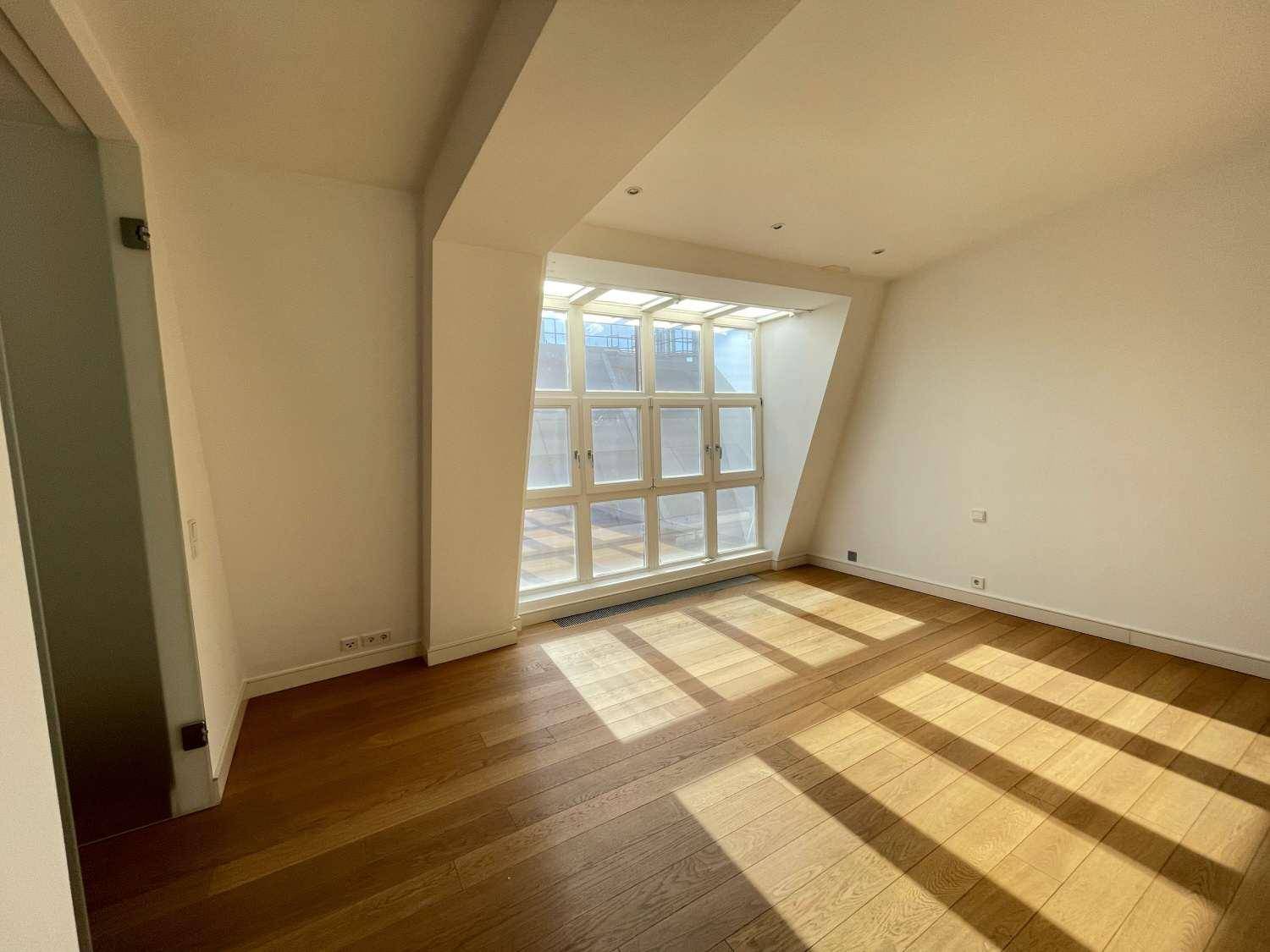 Helles Zimmer mit Holzboden und einer großen Fensterfront, die viel Tageslicht hereinlässt.