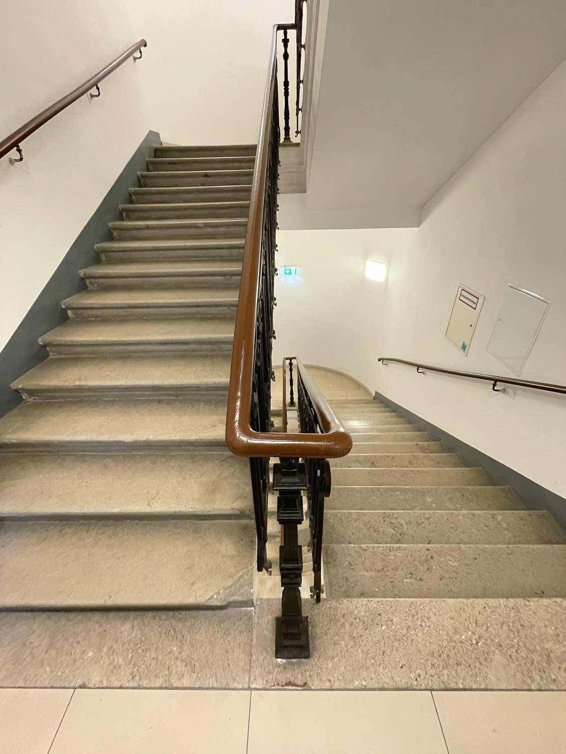 Klassisches Treppenhaus mit Steinstufen und einem eleganten Holzgeländer in einem historischen Gebäude.