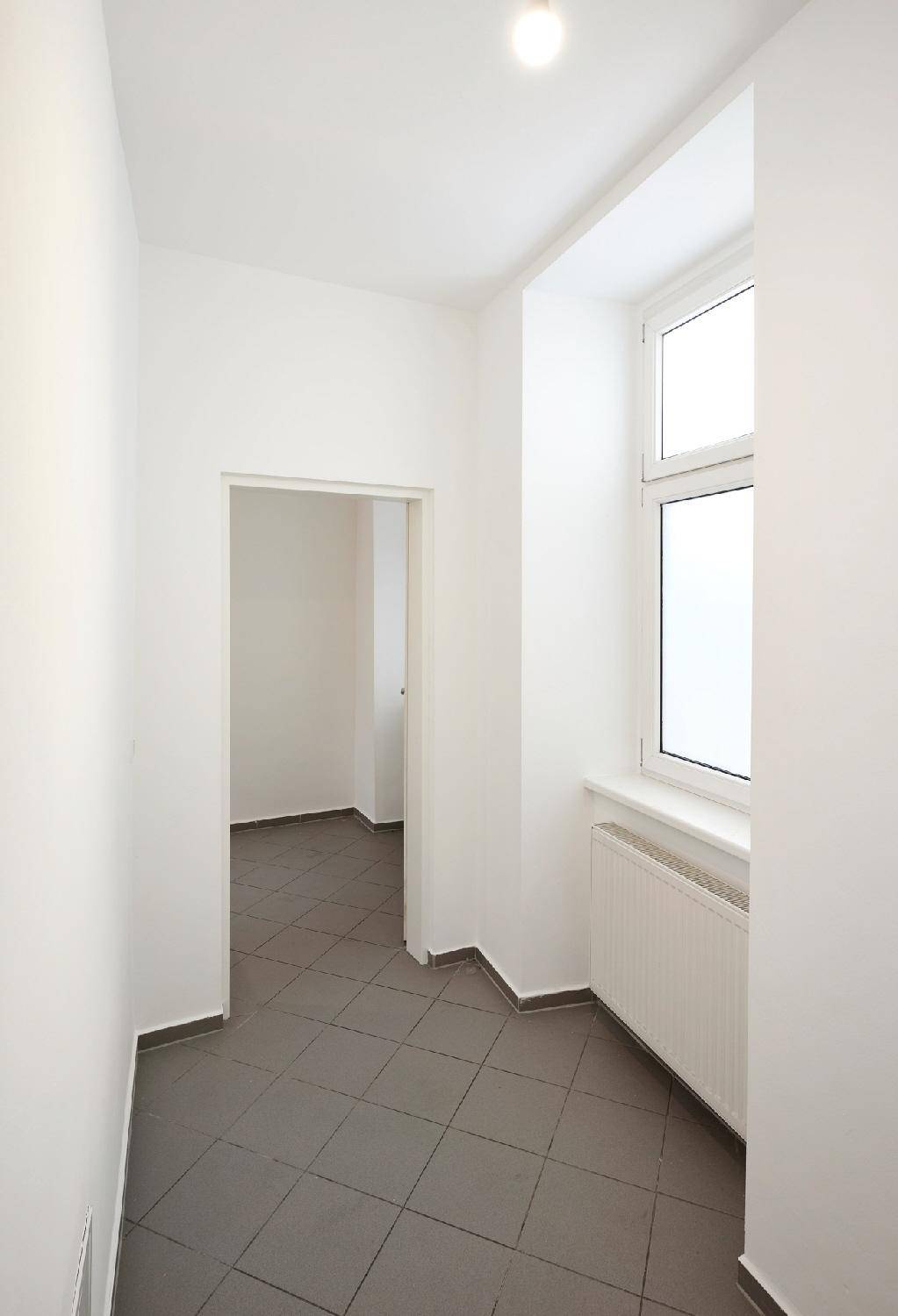 Heller Flur mit grauen Fliesenboden und einem Fenster, das Tageslicht spendet.