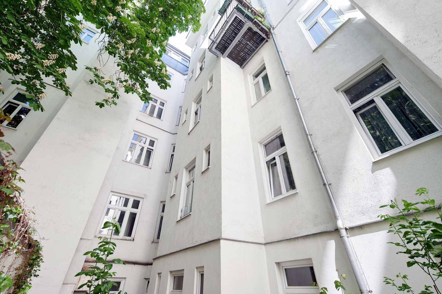 Heller Innenhof eines Wohnhauses mit grünen Pflanzen und einem kleinen Balkon.