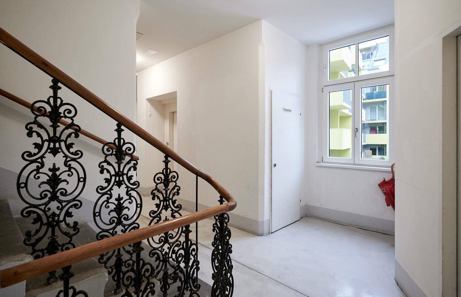 Heller Treppenabsatz mit Fenster und schmiedeeisernem Geländer in einem Altbau.