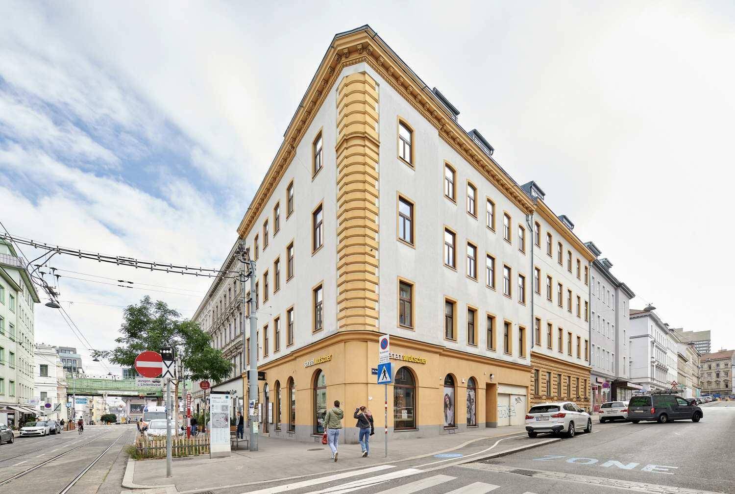 Großes Eckgebäude mit markanter Architektur an einer belebten Stadtstraße unter blauem Himmel.