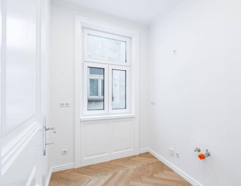 Kleiner Raum mit Fenster, Fischgrätparkett und Anschlüssen für eine mögliche Nutzung als Hauswirtschaftsraum.