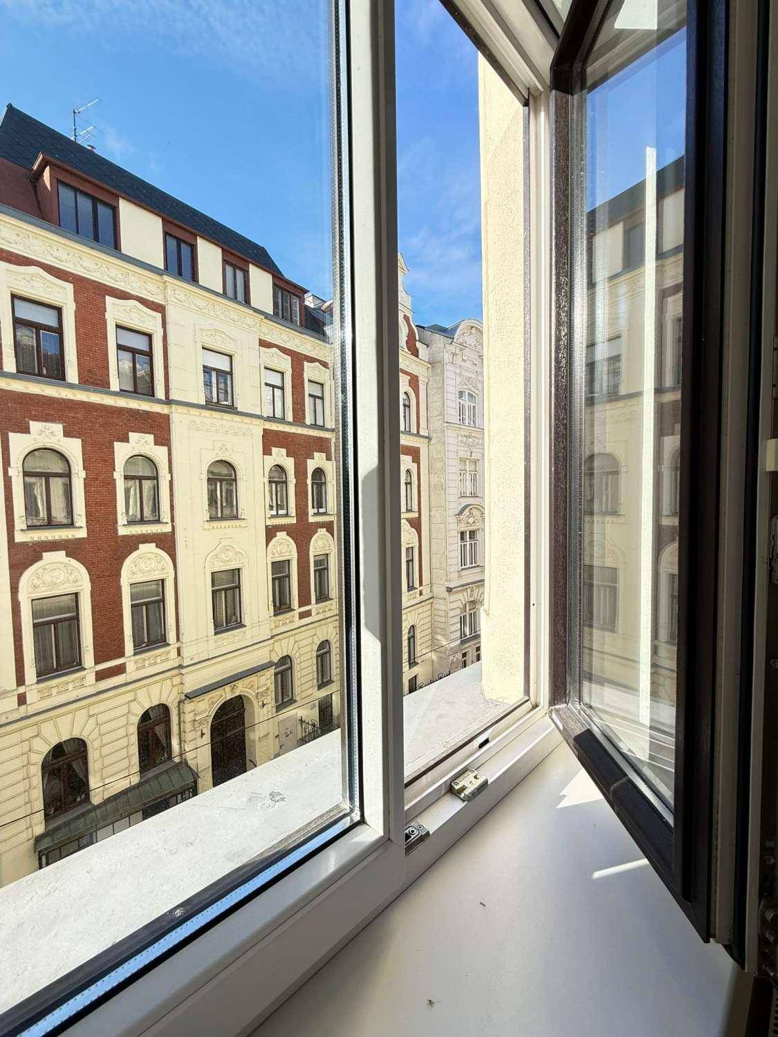 Blick aus dem Fenster auf die historische Fassade eines gegenüberliegenden Gebäudes in der Stadt.