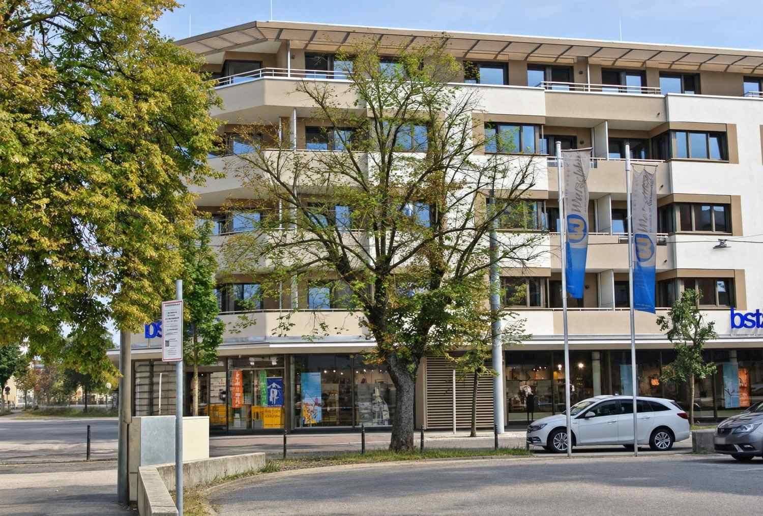 Modernes Gebäude mit mehreren Balkonen und großen Fenstern, umgeben von Bäumen.