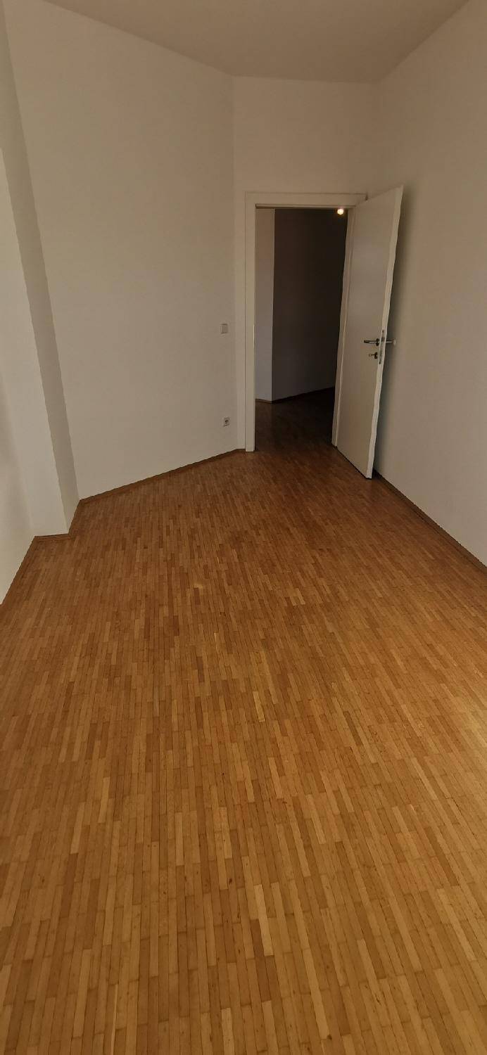 Schlichter Flur mit Holzparkett und weißen Wänden, der zu den angrenzenden Zimmern führt.