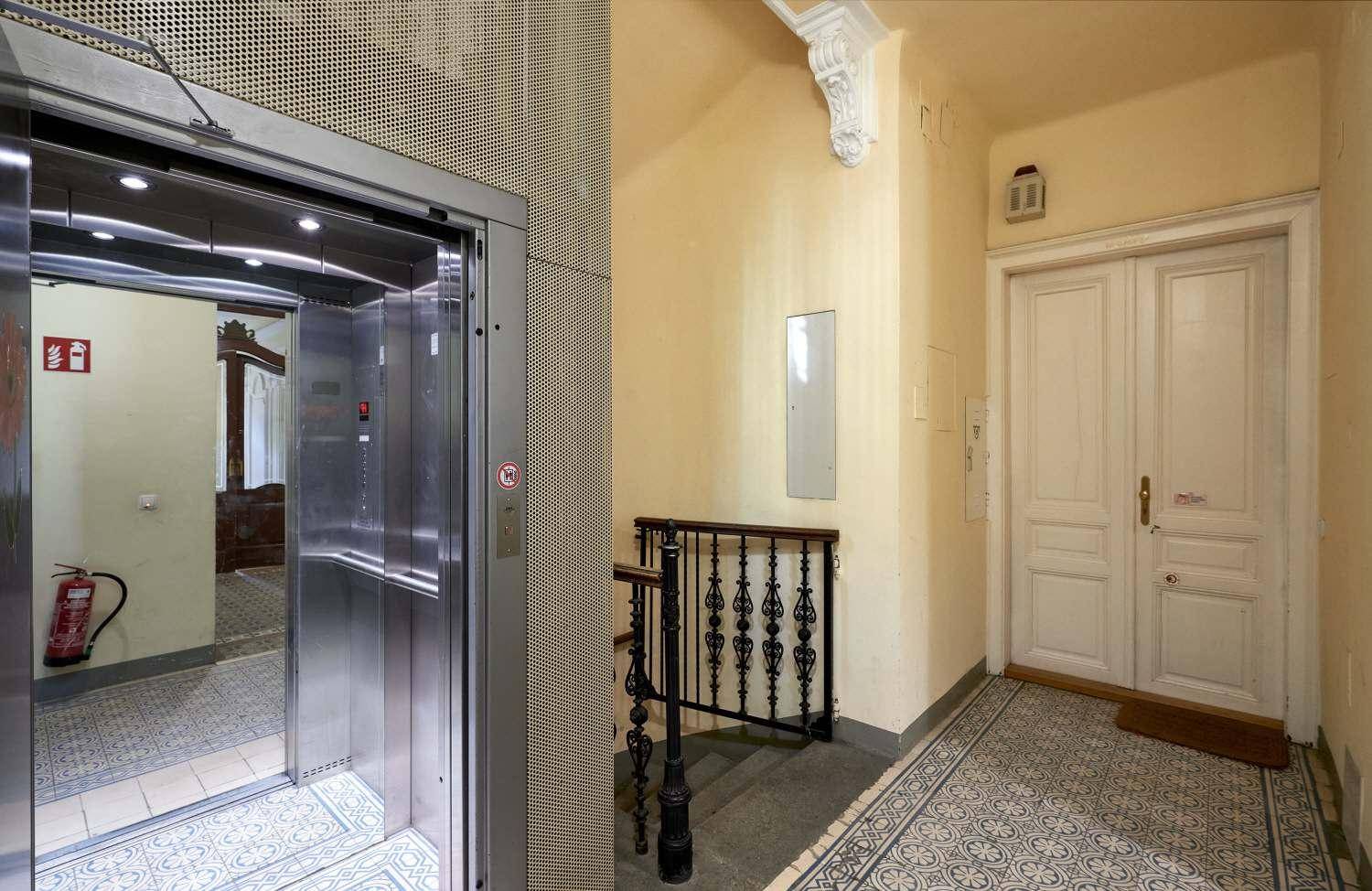Detailansicht des modernen Aufzugs im historischen Treppenhaus mit gemusterten Bodenfliesen und Doppeltür.
