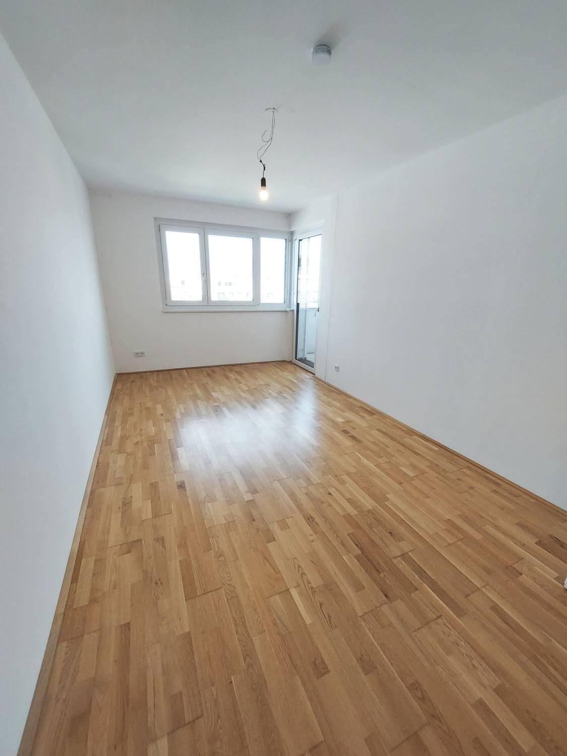 Helles Schlafzimmer mit Parkettboden und Zugang zum Balkon.