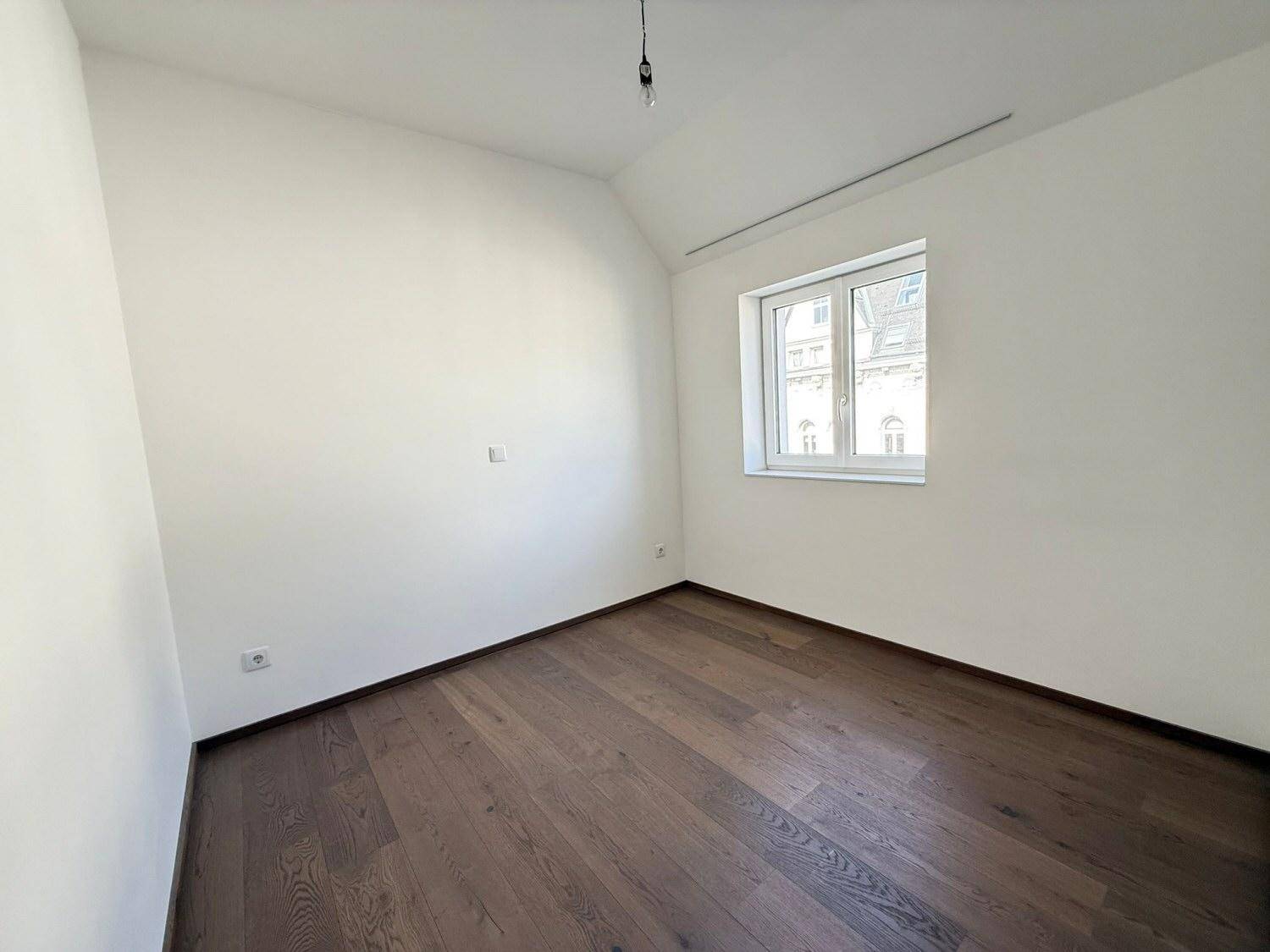 Ruhiges Zimmer mit Holzboden und einem Fenster, ideal als Schlafzimmer oder Arbeitszimmer.