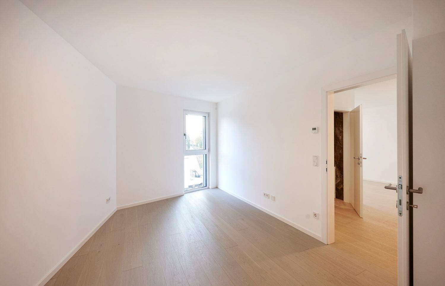 Leeres Schlafzimmer mit hellem Parkettboden und großem Fenster.