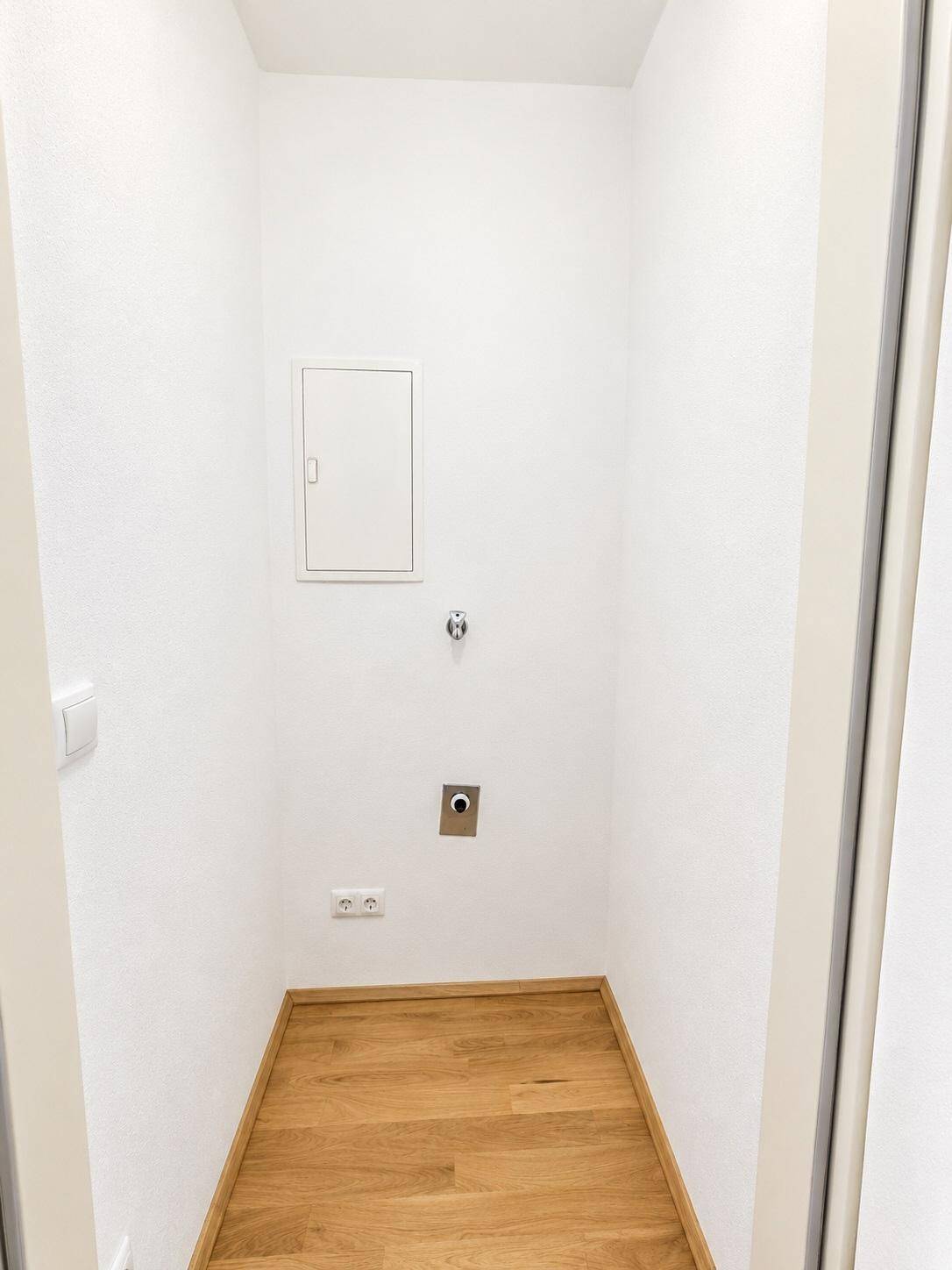 Praktischer Abstellraum mit Anschlüssen für eine Waschmaschine und Holzboden.