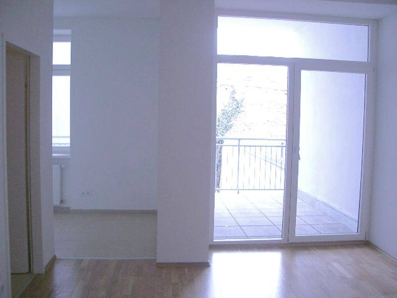 Heller Raum mit Holzboden und Zugang zu einem Balkon, ideal für Wohn- oder Schlafzimmer.