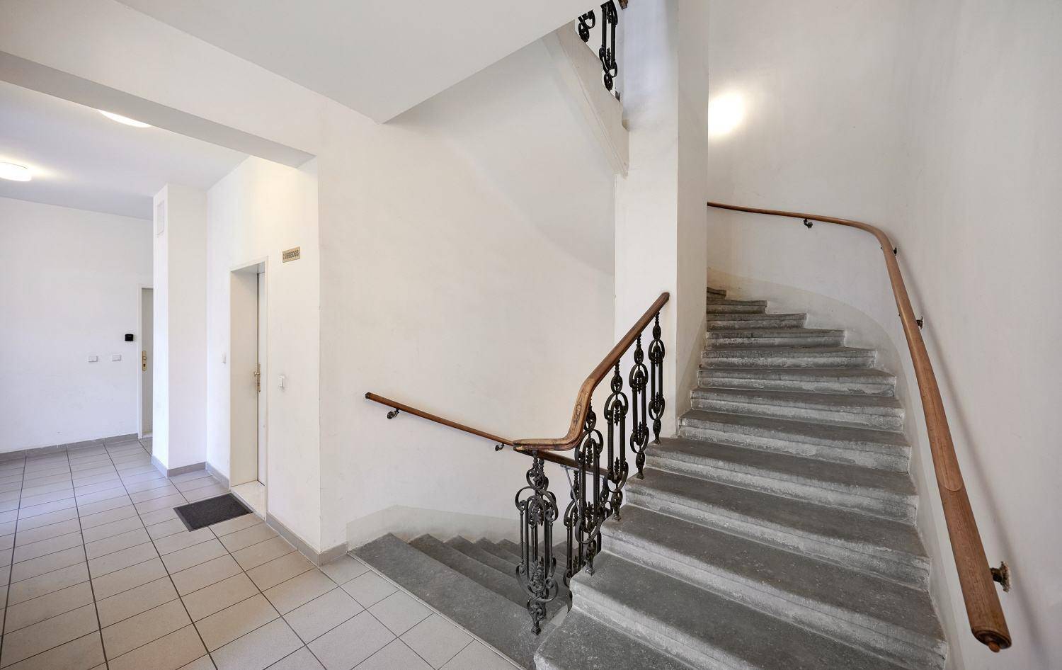 Elegantes Treppenhaus mit Steinstufen und kunstvollem Geländer in einem klassischen Altbau.