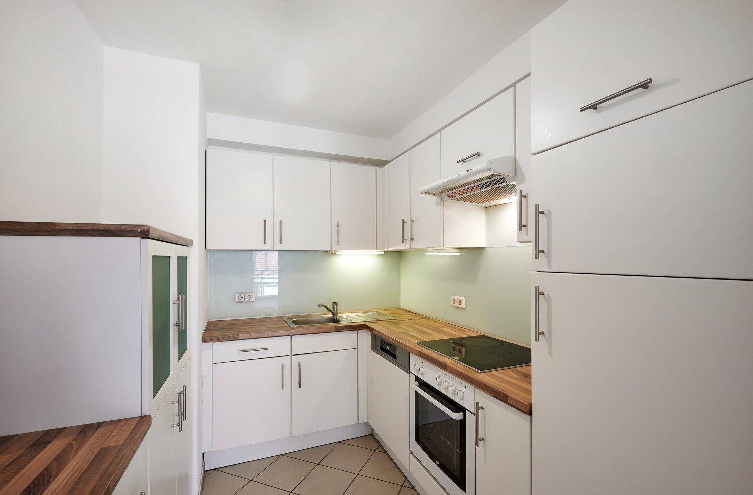 Funktionale Küche mit weißen Schränken, Holz-Arbeitsplatten und integrierten Geräten, ideal für den täglichen Gebrauch.