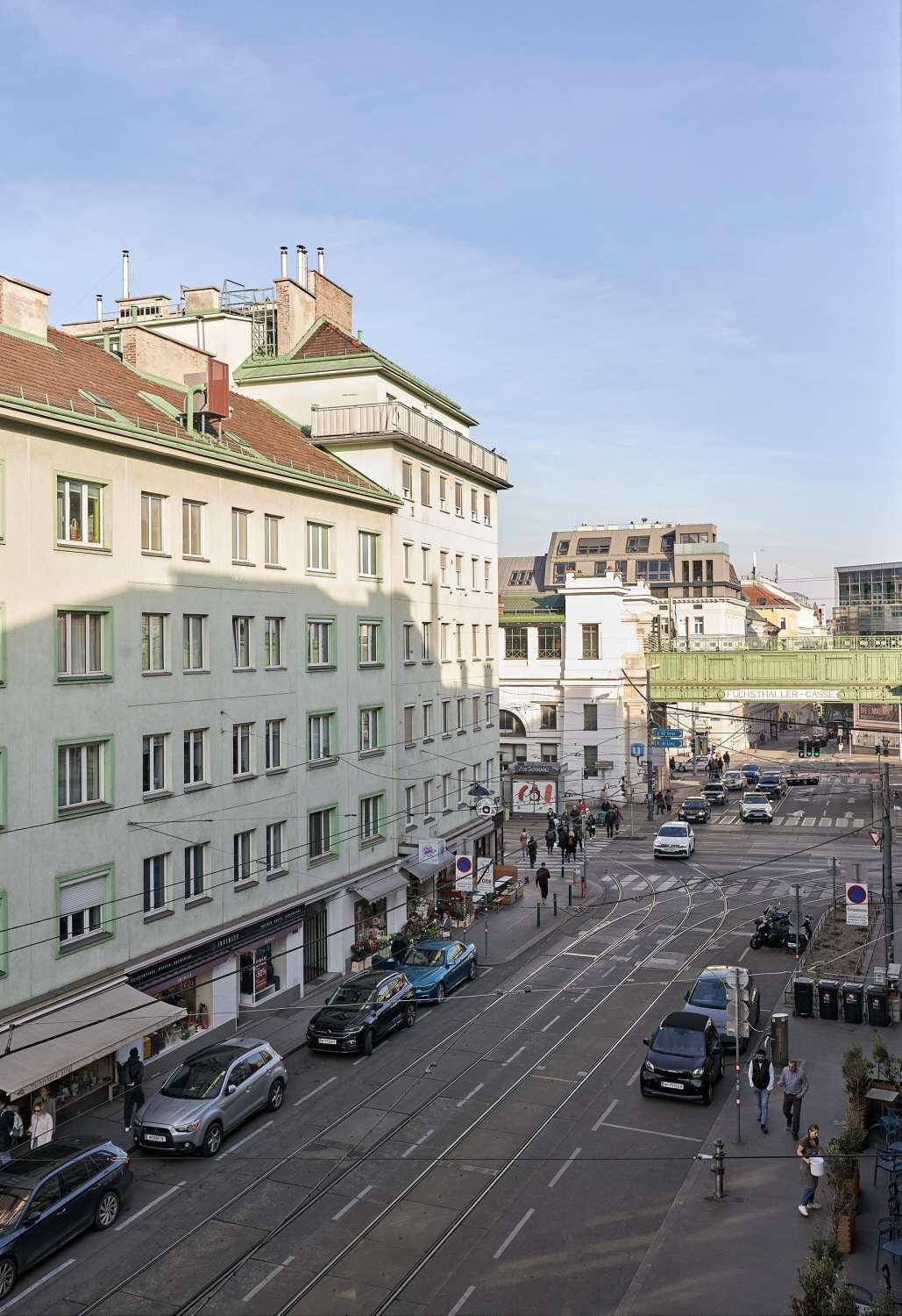 Panoramablick auf eine belebte Stadtstraße mit Gebäuden, Verkehr und grünen Dächern im Hintergrund.