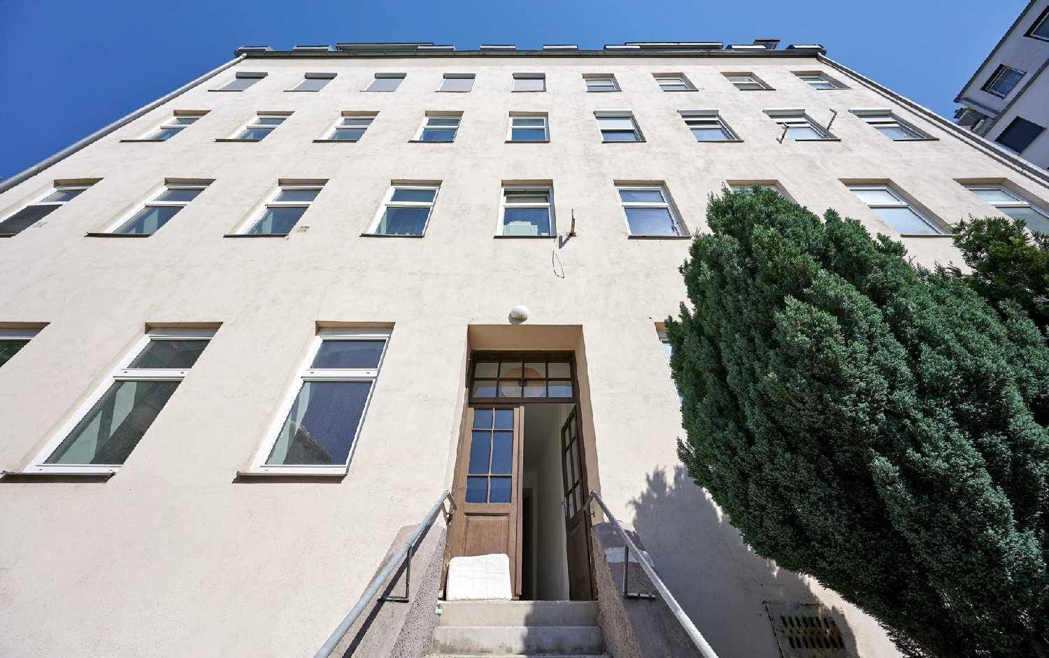 Die Fassade des Gebäudes mit vielen Fenstern und dem Eingangsbereich unter blauem Himmel.