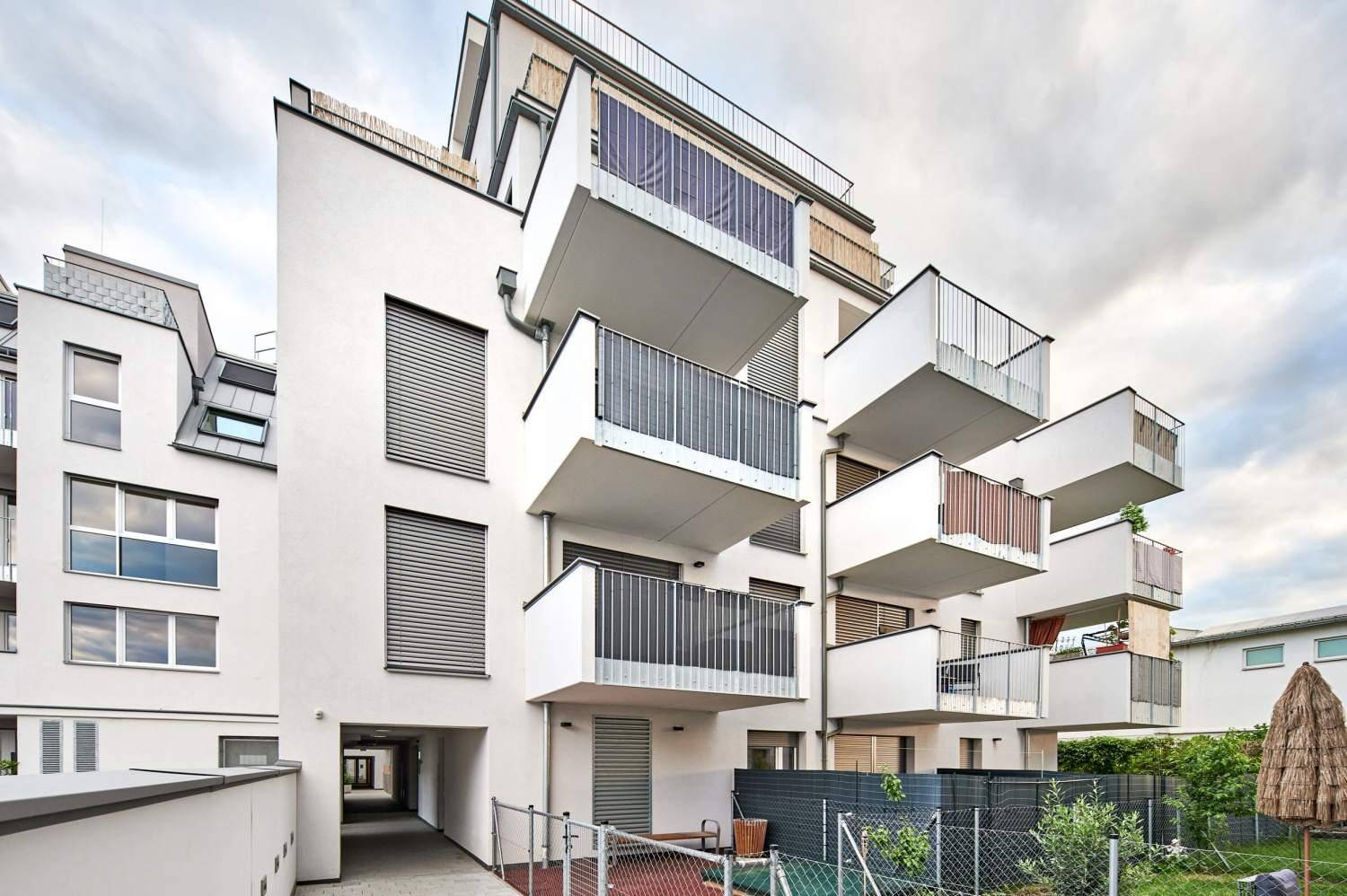 Modernes Wohngebäude mit Balkonen und einem kleinen, gepflegten Gartenbereich.