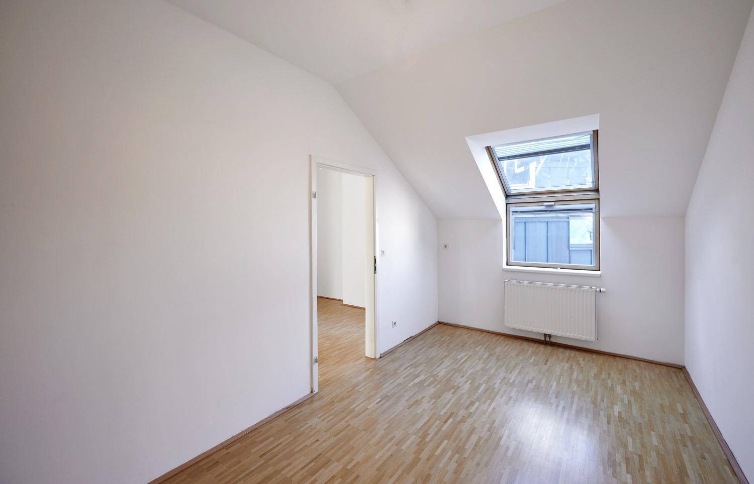 Kleines Zimmer mit Dachschräge, Holzboden und einem Dachfenster.