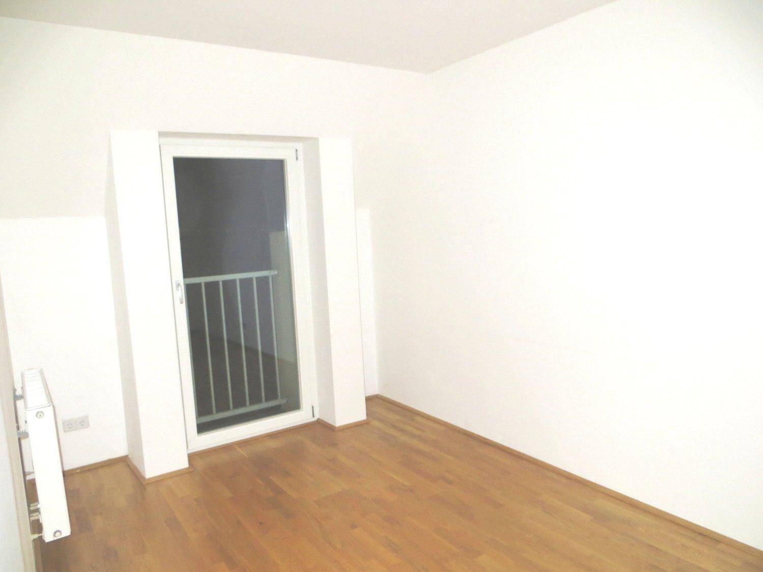 Helles Zimmer mit Parkettboden und Zugang zu einem französischen Balkon.