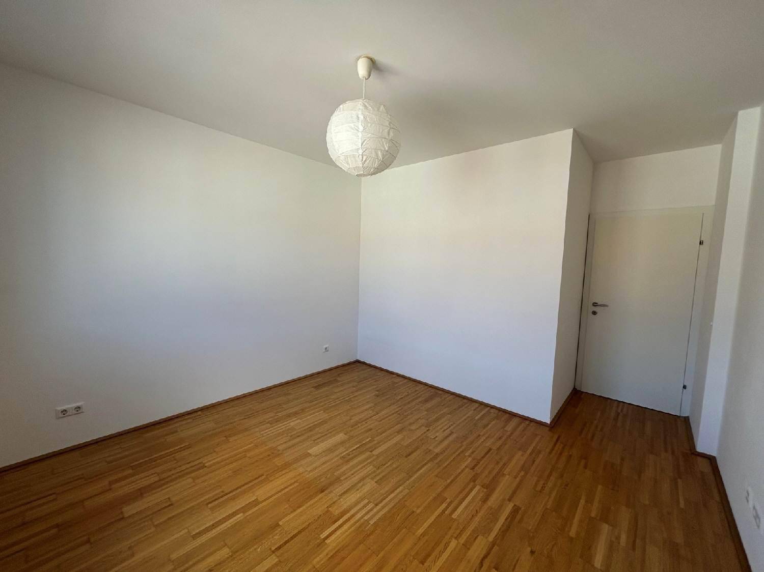 Leeres Zimmer mit hellem Parkettboden und weißen Wänden, bereit zur individuellen Gestaltung.
