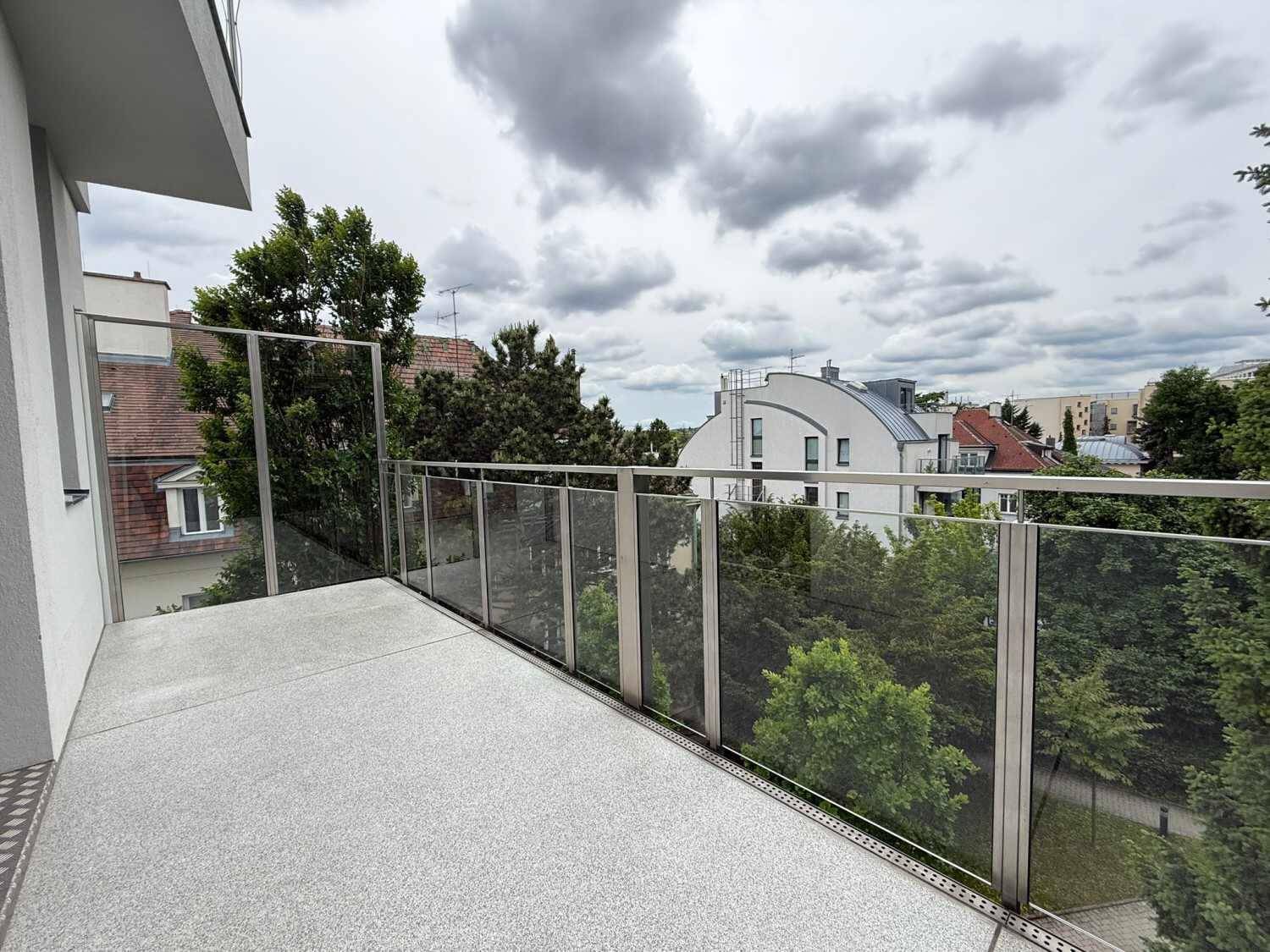 Moderner Balkon mit Glasgeländer und weitem Blick über grüne Bäume und Gebäude.