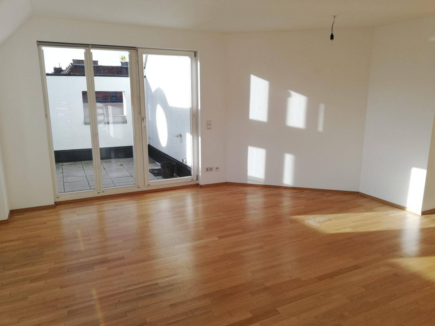 Geräumiger, heller Wohnraum mit Holzboden und großzügigem Zugang zu einer sonnigen Terrasse.