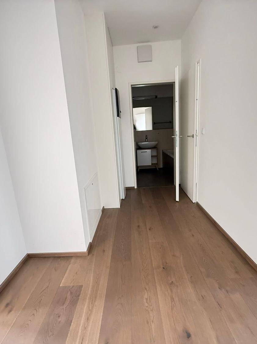 Heller Flur mit Holzboden, der zu einem Badezimmer mit Waschbecken und Spiegel führt.