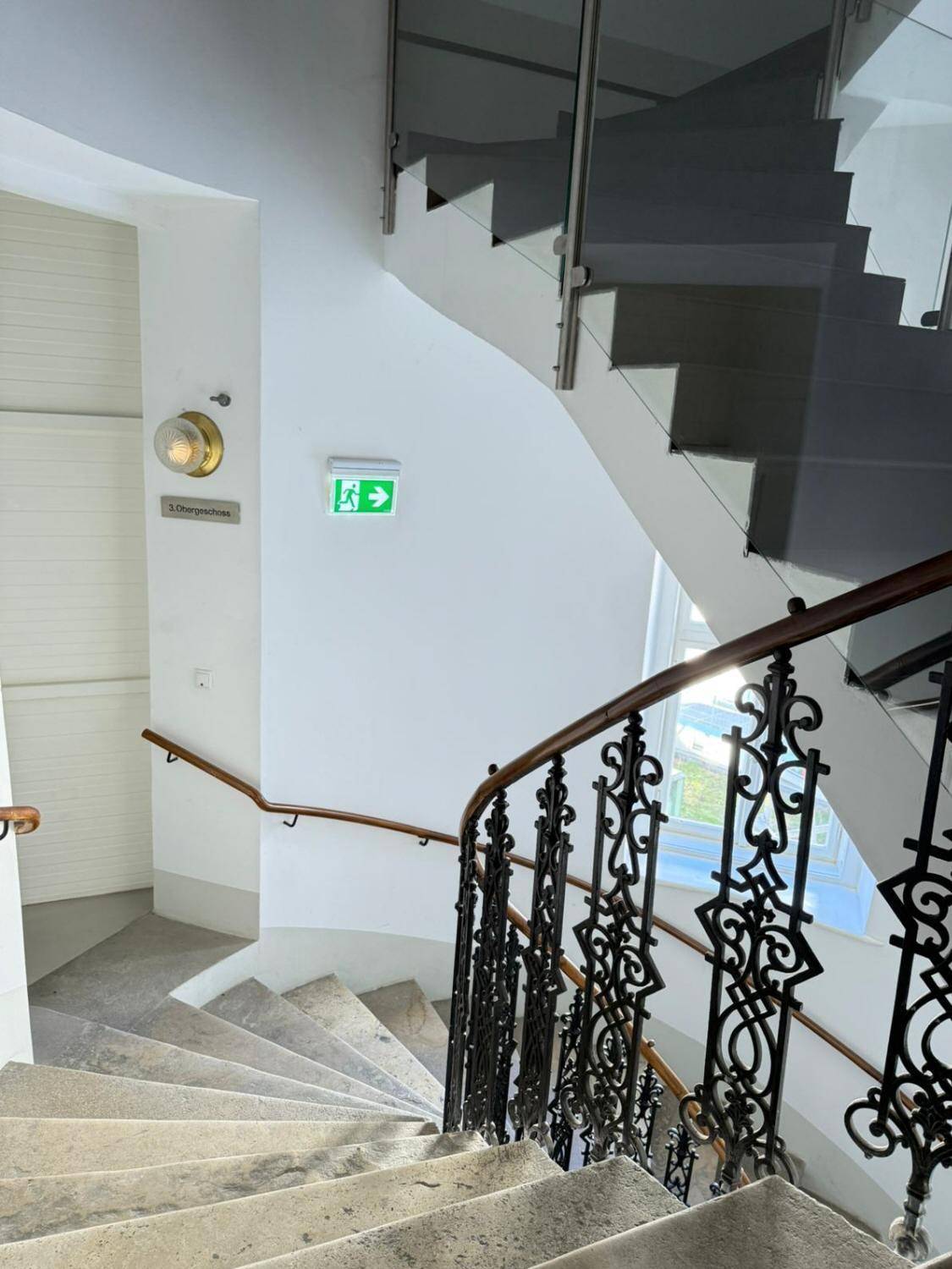 Historisches Treppenhaus mit schmiedeeisernem Geländer und Steinstufen in einem Altbau.