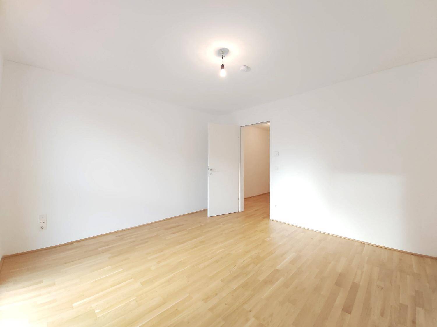 Leeres Zimmer mit hellem Parkettboden und weißen Wänden, bereit zur individuellen Gestaltung.