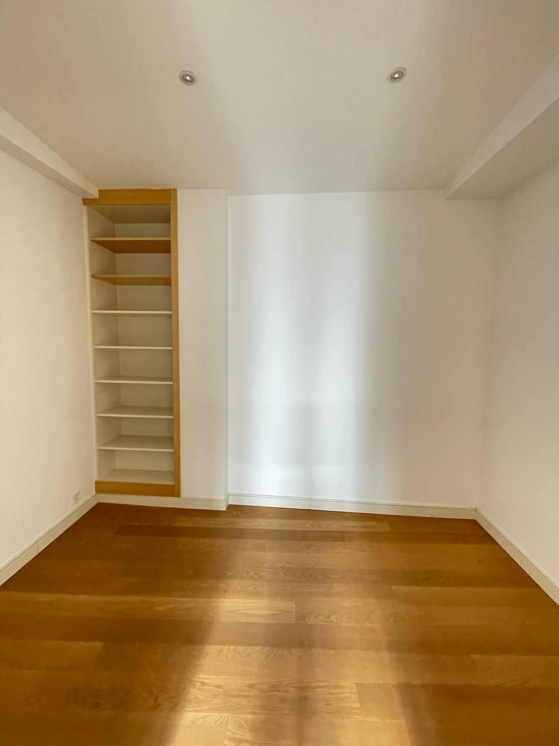 Helles Zimmer mit Holzboden und einem praktischen Einbauregal, vielseitig nutzbar.