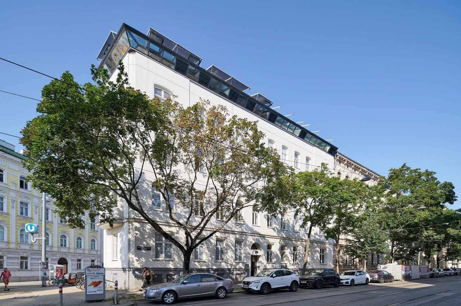 Modernisiertes Eckgebäude mit Solarpaneelen auf dem Dach und Bäumen entlang der Straße.