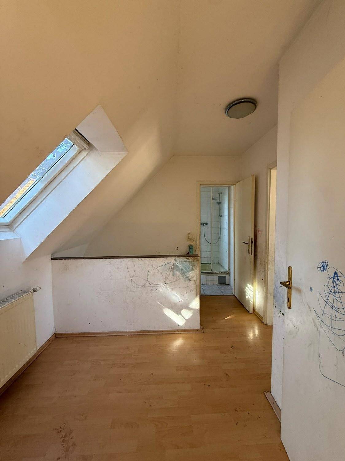 Dachgeschosszimmer mit Dachfenster und Zugang zu einem Badezimmer, renovierungsbedürftig.