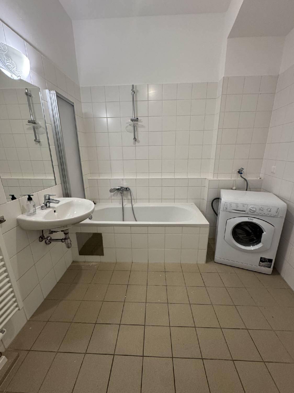 Badezimmer mit Badewanne, Waschbecken, Fliesenboden und einer Waschmaschine, in gutem Zustand.