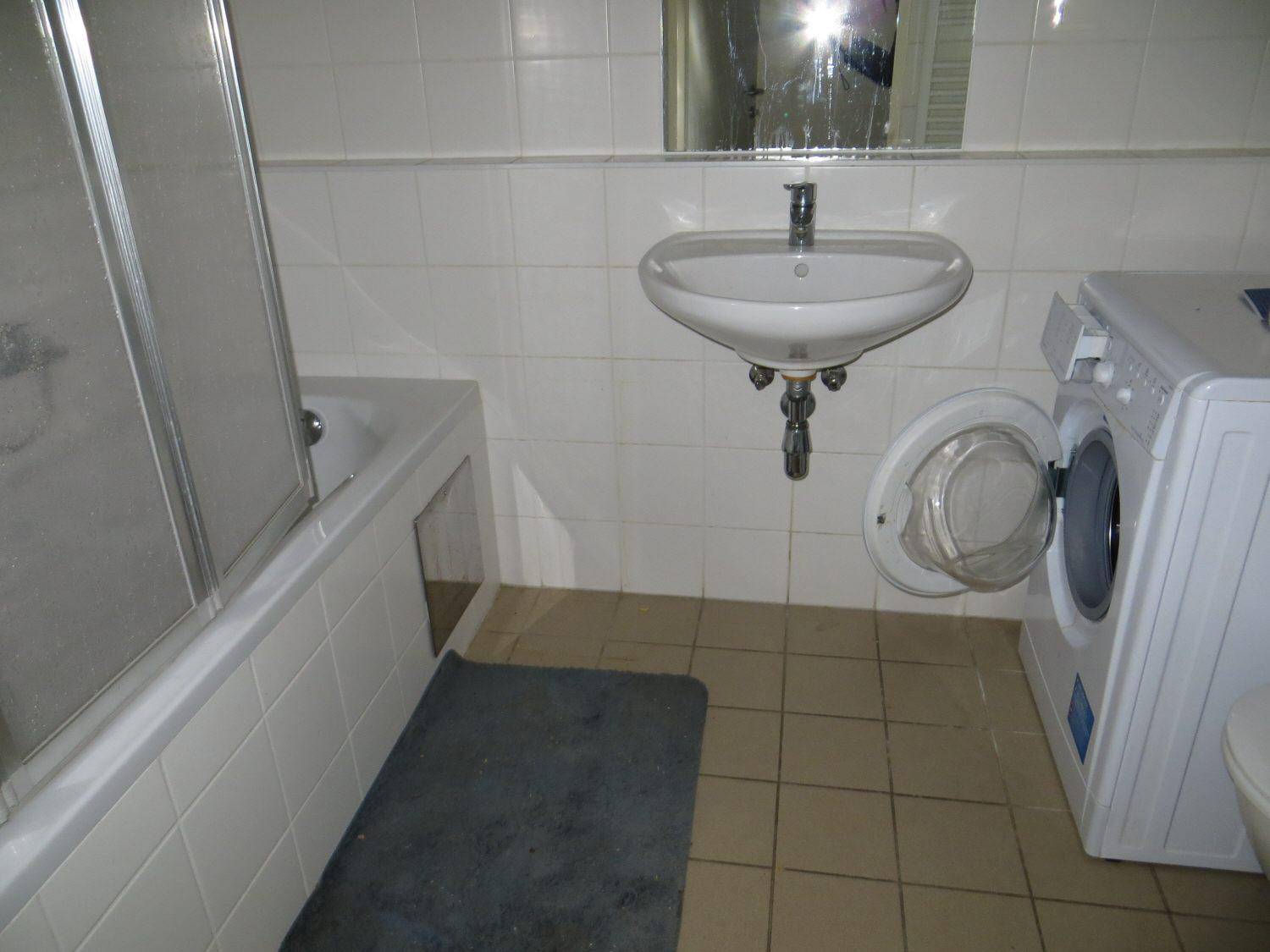 Badezimmer mit Badewanne, Waschbecken, Waschmaschine und weißen Fliesen.