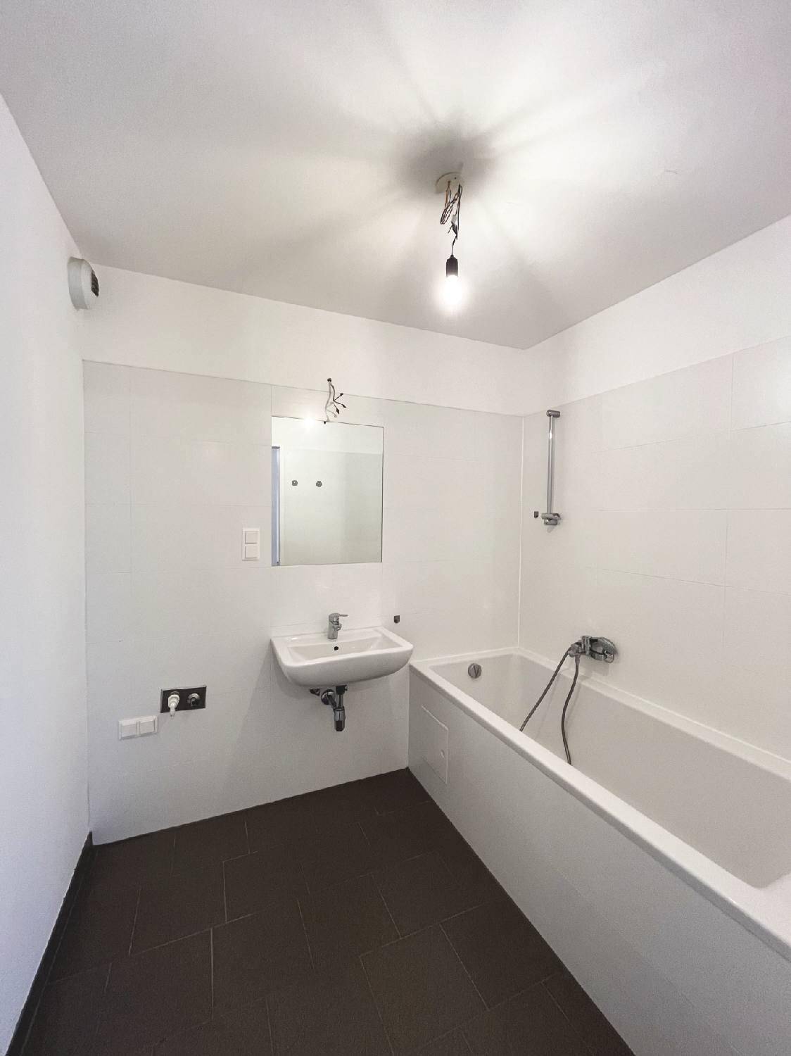 Funktionales Badezimmer mit Badewanne, Waschbecken und dunklen Fliesen, ergänzt durch helle Wandfliesen.