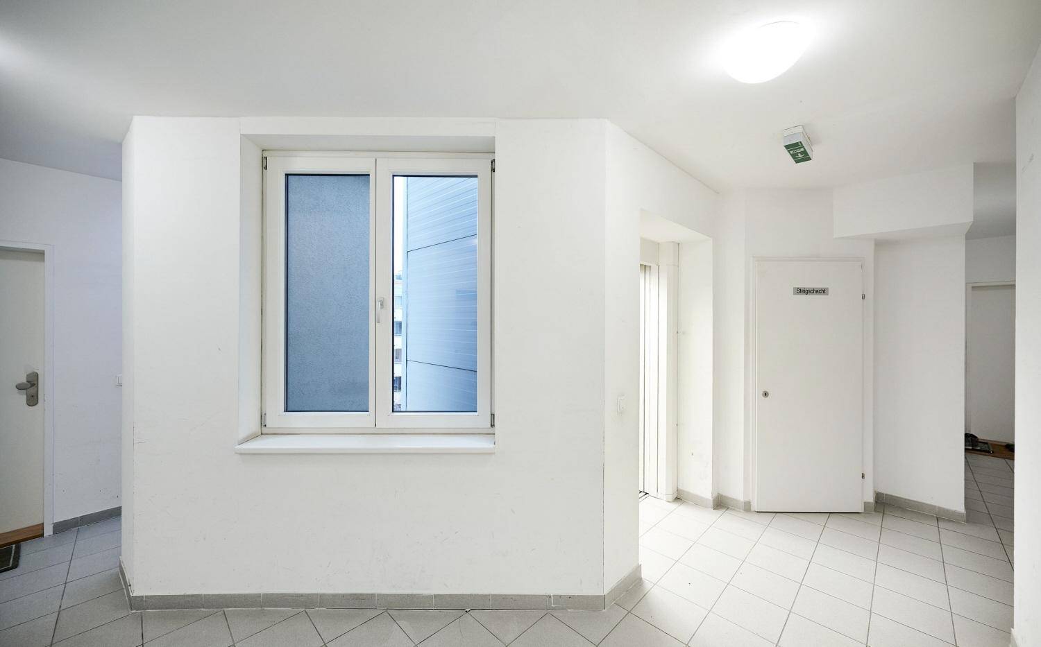 Heller Eingangsbereich mit Fliesenboden, großem Fenster und Zugangstüren zu den Wohnungen.