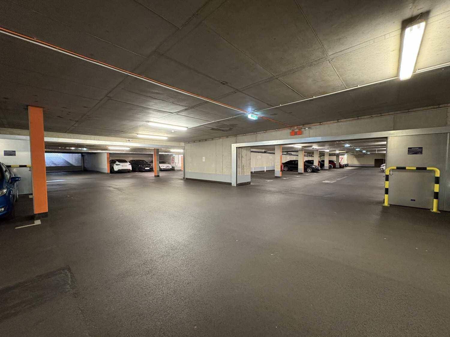 Geräumige Tiefgarage mit guter Beleuchtung und gelb-schwarzen Schutzbügeln.