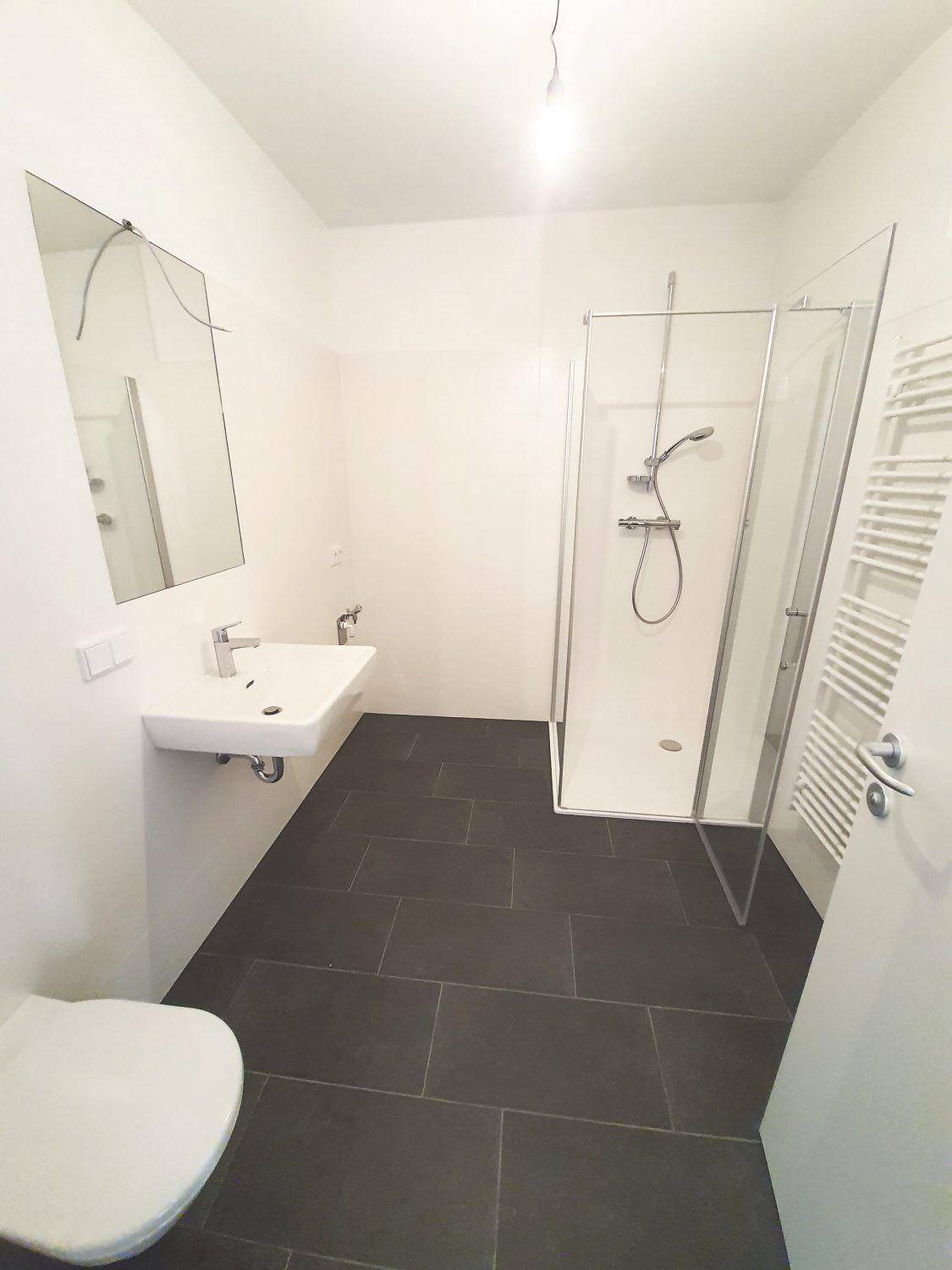 Modernes Badezimmer mit dunklen Fliesen, Dusche, Waschbecken und Handtuchheizkörper.