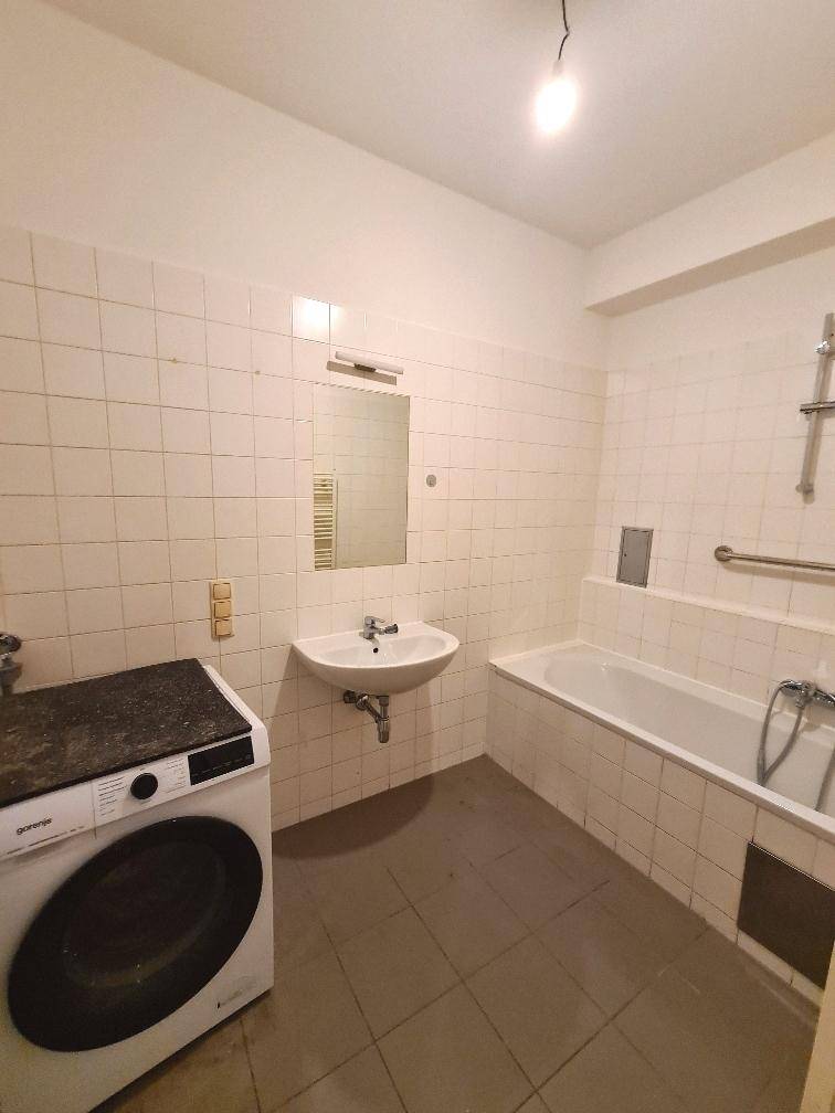 Badezimmer mit Badewanne, Waschbecken und Waschmaschine, ausgestattet mit hellen Wandfliesen.