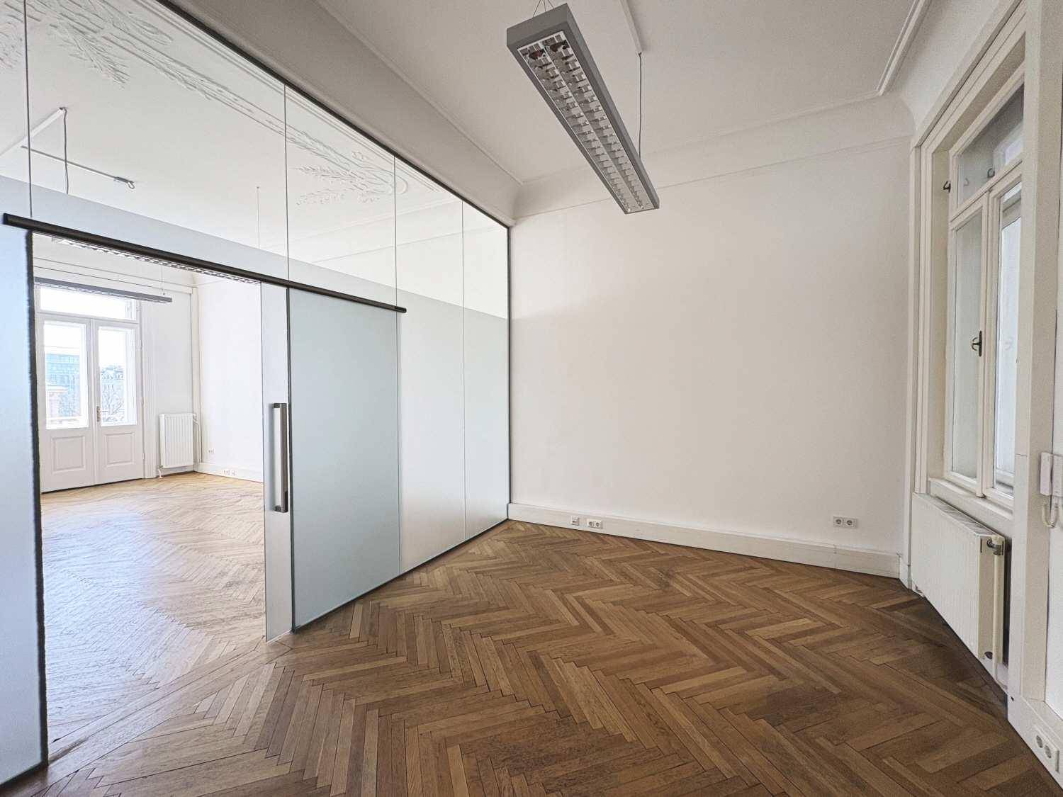 Helles Zimmer mit Fischgrätparkett und moderner Glastrennwand, bietet flexible Raumnutzung.