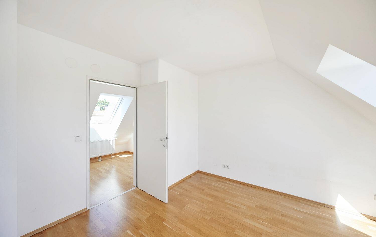 Geräumiges Schlafzimmer im Dachgeschoss mit Holzboden und einem Dachfenster, hell und ruhig.