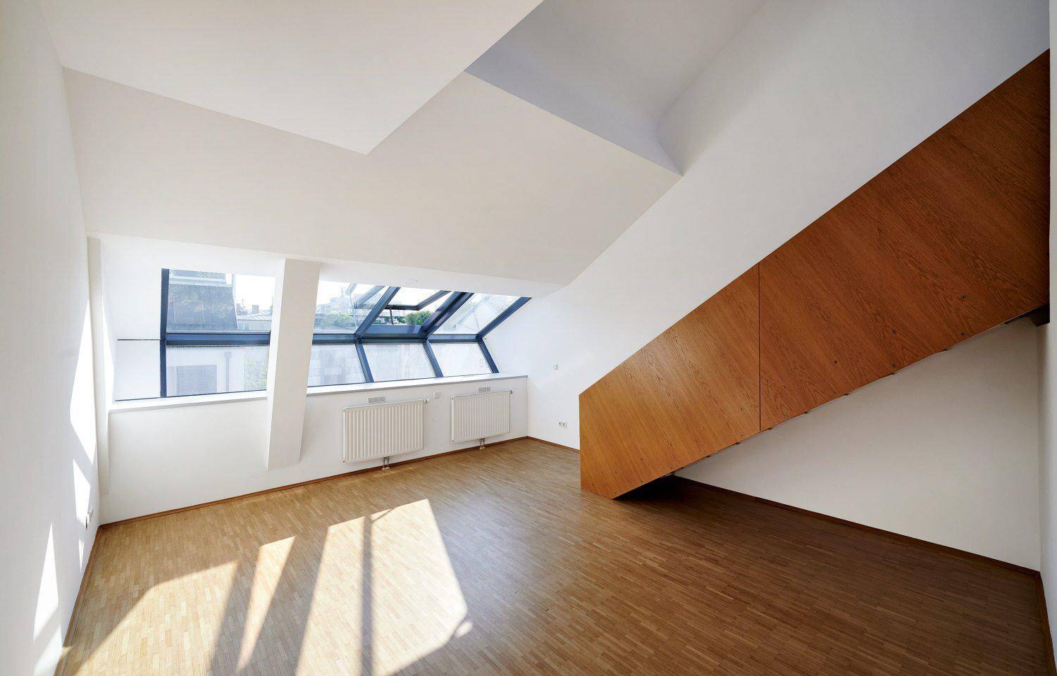 Heller Wohnbereich mit Holzparkett, hohen Decken und großen Dachfenstern für viel Tageslicht.
