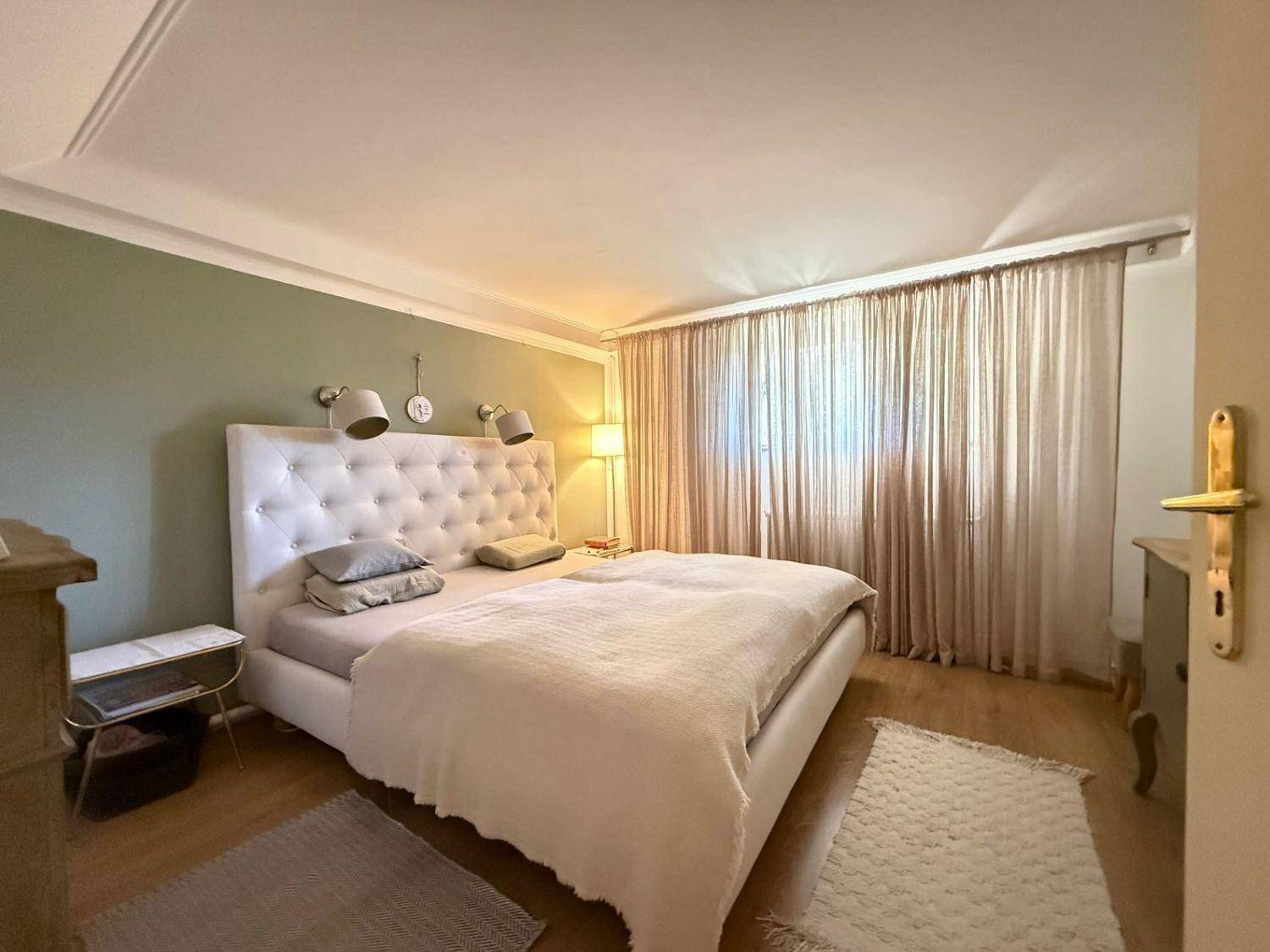 Gemütliches Schlafzimmer mit großem Doppelbett, Parkettboden und hellen Vorhängen.