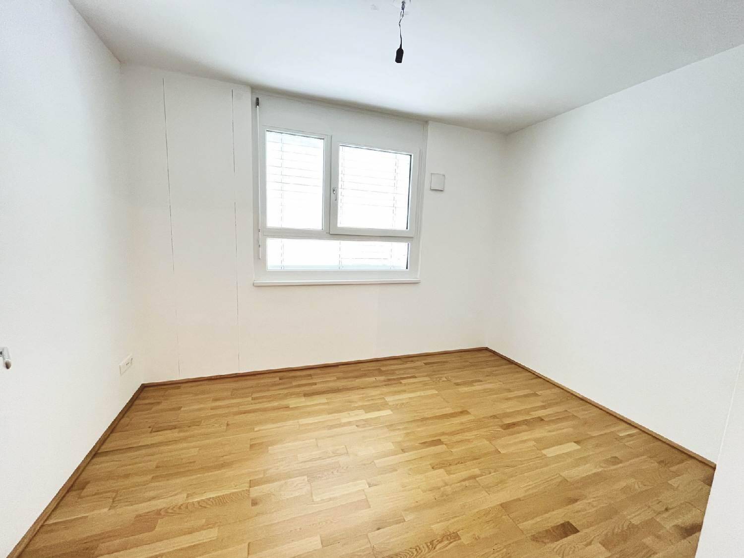 Helles Schlafzimmer mit Parkettboden und einem großen Fenster für viel Tageslicht.