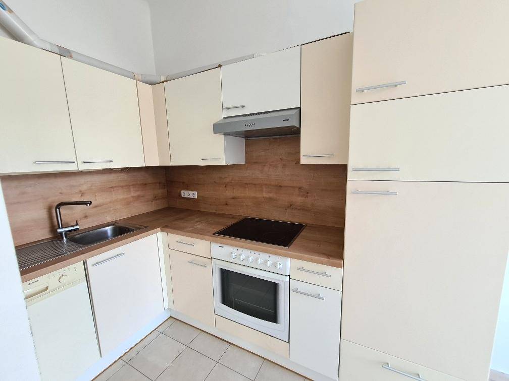 Funktionale Einbauküche in hellem Beige mit Holzoptik-Arbeitsplatte und Fliesenboden.