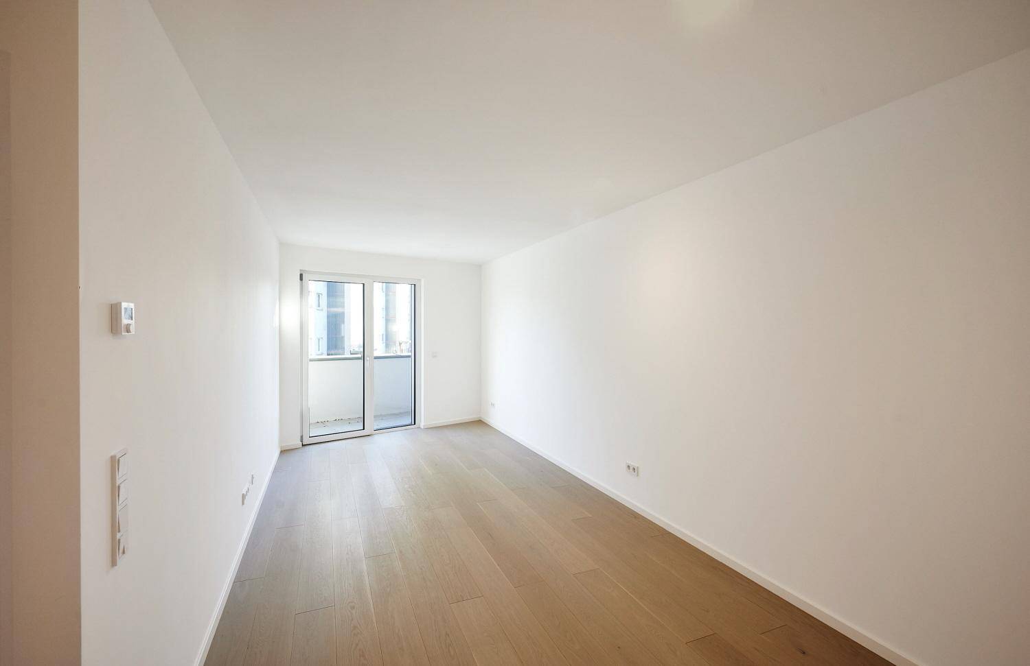 Geräumiges Schlafzimmer mit Parkettboden und Zugang zum Balkon.