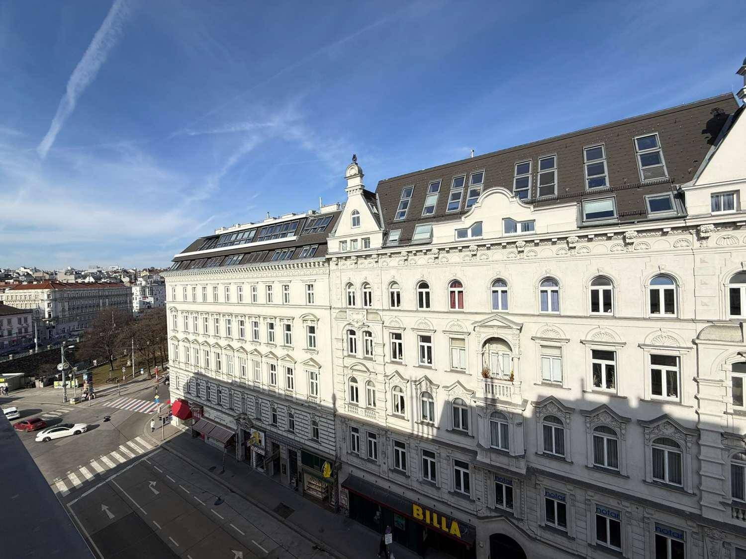 Weitläufiger Blick auf eine belebte Stadtstraße mit historischen Gebäuden und Geschäften.