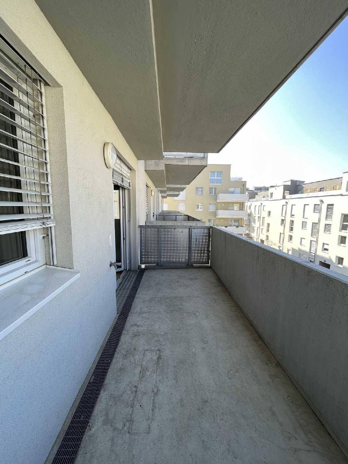 Schmaler Balkon mit Betonboden und Blick auf die moderne Wohnbebauung.