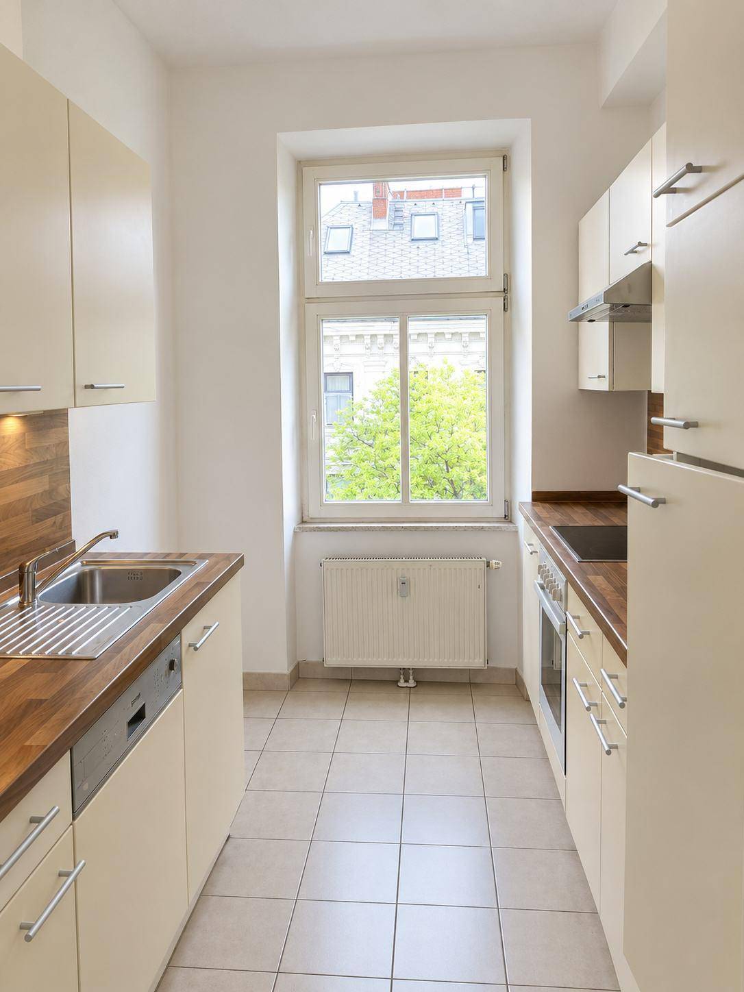 Funktionale Küche mit hellen Schränken, Holz-Arbeitsplatten und Fenster, inklusive Spülmaschine.