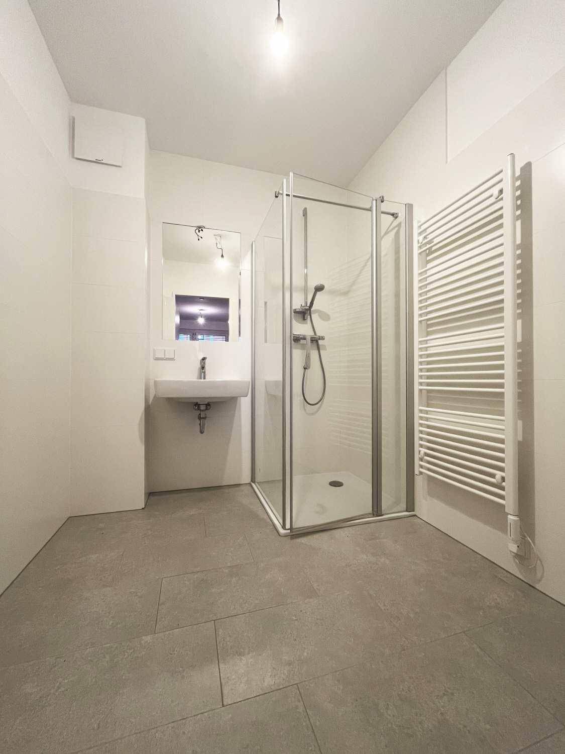 Modernes Badezimmer mit grauen Fliesen, Duschkabine und beheiztem Handtuchhalter.